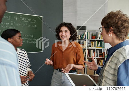 Diverse group of adults engaged in discussing educational concepts in casual office setting, with chalkboard in background showing informational notes 119707665