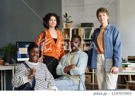 Group photo of diverse team members posing together in modern office environment. Open shelving and computer equipment in the background creating a professional yet casual atmosphere Group photo of diverse team members posing together in modern office environment. Open shelving and computer equipment in the background creating a professional yet casual atmosphere 119707805