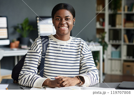 Portrait of smiling African American woman sitting at office desk with a relaxed and confident expression, featuring organized workspace background, reflecting work environment 119707808