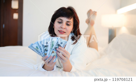 Rich beautiful woman counting cash while lying in bed in hotel Rich beautiful woman counting cash while lying in bed in hotel 119708121