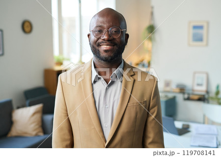 Waist up portrait of adult Black man wearing suit and smiling brightly at camera standing indoors in home interior, copy space 119708141