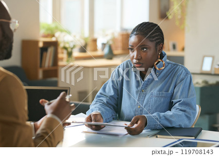 Portrait of young African American woman holding documents and talking to finance expert during finance and taxes consultation at home copy space 119708143