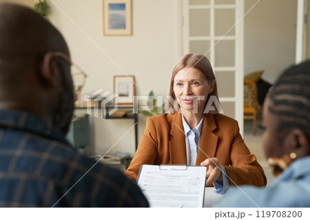 Portrait of smiling mature woman as finance expert handing contract on clipboard to clients during consultation copy space Portrait of smiling mature woman as finance expert handing contract on clipboard to clients during consultation copy space 119708200