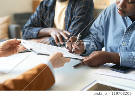 Close up of African American woman signing contract on clipboard during consultation with insurance agent or financial advisor in office copy space 119708209