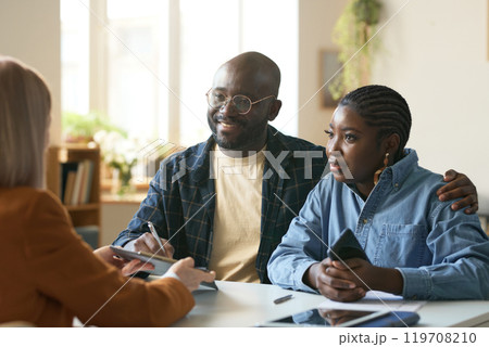Portrait of smiling African American couple enjoying consultation with insurance agent sitting at desk in office and signing forms copy space Portrait of smiling African American couple enjoying consultation with insurance agent sitting at desk in office and signing forms copy space 119708210