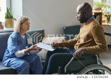 Side view portrait of African American man with disability signing medical form during at home doctors visit copy space 119708266