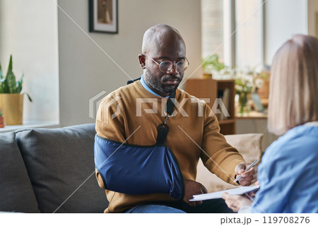 Portrait of adult African American man with broken arm signing contract for at home medical services on clipboard copy space Portrait of adult African American man with broken arm signing contract for at home medical services on clipboard copy space 119708276