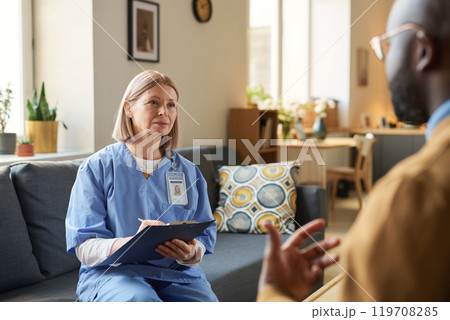 Portrait of adult female doctor listening to patient and holding clipboard during at home visit filling in patient card copy space Portrait of adult female doctor listening to patient and holding clipboard during at home visit filling in patient card copy space 119708285