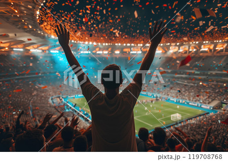 Enthusiastic crowd cheering during thrilling football match in large stadium with colorful confetti falling from sky and bright lights illuminating field 119708768