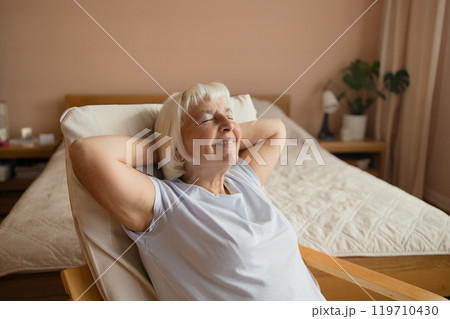 Calm senior woman relaxing on soft comfortable chair having daytime nap, carefree middle aged female breathing fresh air enjoying no stress free peaceful weekend resting  119710430