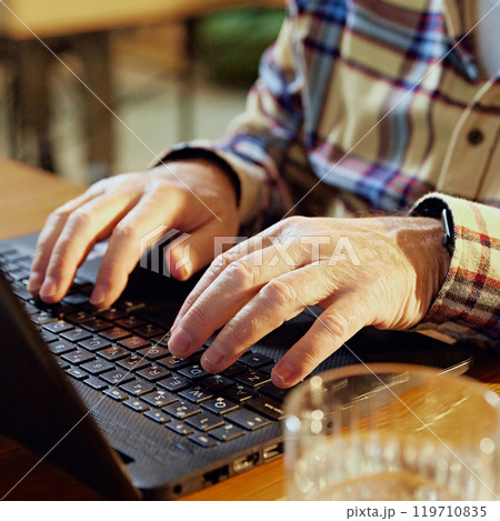 Close up photo of elderly man, dressed casual attire, typing on laptop keyboard sitting at desk in collaborative workspace 119710835