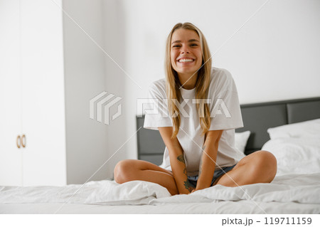 A Joyful and Happy Young Woman Sitting Comfortably on Her Bed in a Cozy Bedroom Space 119711159