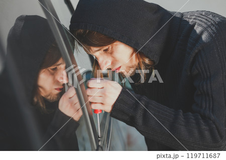Thieft man holding screwdriver breaking into car 119711687