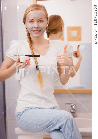 Happy young woman applying mud mask on face 119711853