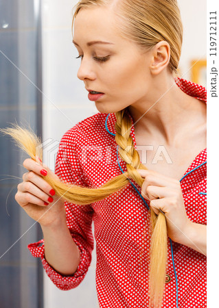 Blonde woman looking at her hair ends Blonde woman looking at her hair ends 119712111