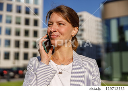 A confident businesswoman is actively engaged in a phone call while outdoors in a cityscape 119712383