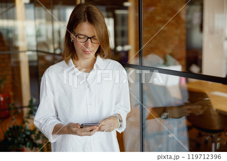 A woman is utilizing her smartphone in a modern office environment that promotes productivity 119712396