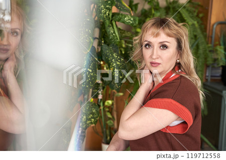 Woman with blonde hair posing indoors near green plants and reflective surface Woman with blonde hair posing indoors near green plants and reflective surface 119712558