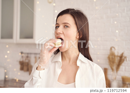 Woman enjoying macarons in kitchen with sparkling lights and cozy decor Woman enjoying macarons in kitchen with sparkling lights and cozy decor 119712594