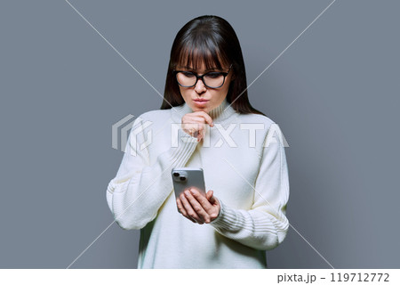 Mature serious woman using smartphone, on grey background 119712772