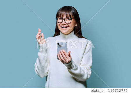 Mature happy woman with smartphone looking at camera, on blue background 119712773
