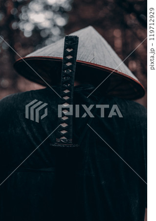 A lone samurai wanders through a dark forest, his trusty katana securely fastened in his hands, representing strength, courage and honor in the serene nature. Samurai with a katana in the forest. 119712929