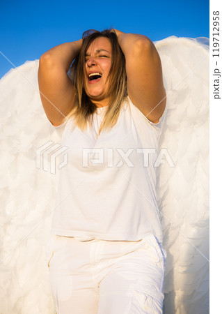 Upset blonde woman with angel wings screaming under blue sky showing stress, frustration, anger and despair but also hope and freedom. Upset blonde woman with angel wings screaming under blue sky showing stress, frustration, anger and despair but also hope and freedom. 119712958