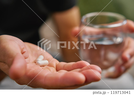 Man holding pills and glass of water at home. Person taking supplements 119713041