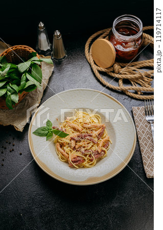 Classic carbonara pasta with Parmesan, basil, and crispy bacon strips, served in an elegant setting 119714117