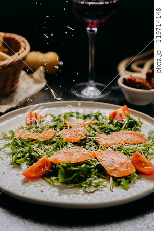 Arugula salad with smoked salmon, cherry tomatoes, and freshly grated Parmesan, served with red wine 119714148