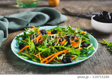 Delicious salad of carrots, arugula and prunes on a plate on the table 119715280