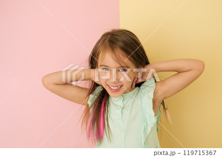 A girl with colored hair laughs merrily looking at the camera on a yellow and pink studio background A girl with colored hair laughs merrily looking at the camera on a yellow and pink studio background 119715367
