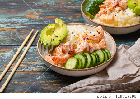 White ceramic bowl with rice, shrimps, avocado, vegetables and sesame seeds and chopsticks on colourful rustic wooden background front view. Healthy asian style poke bowl 119715599