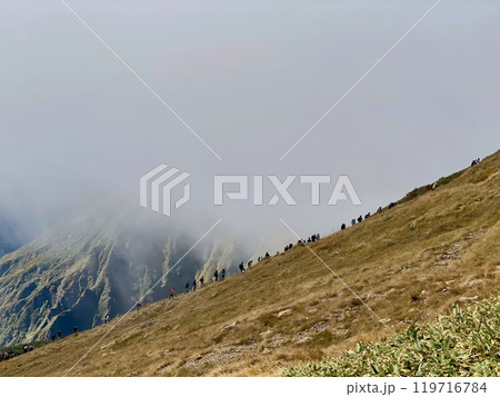 ガスが抜け眺望が開けるのを楽しみに登る登山者の列 119716784