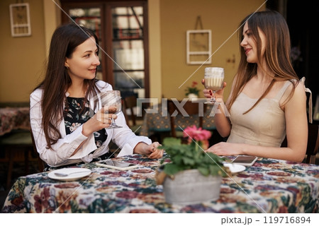 Two women, women sitting, Outdoor Gathering. Two young women having conversation over coffee at outdoor cafe, creating relaxed and friendly atmosphere with warm tones. 119716894