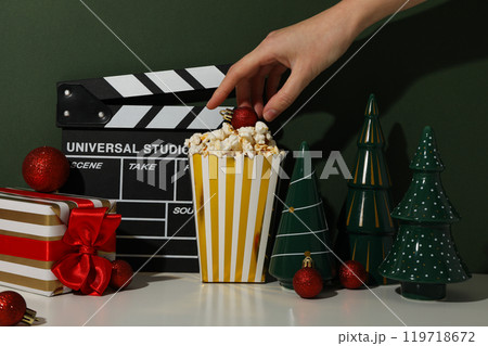 Clapperboard, paper cup with popcorn, hand and Christmas decorations on green background 119718672