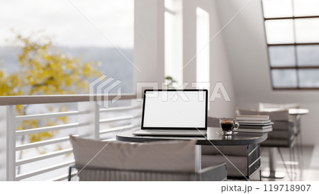 A laptop with a white screen mockup on a table in a modern coffee shop or hotel lounge patio. 119718907