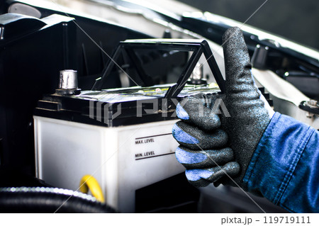Auto mechanic thumbs up with confidence next to car battery 119719111