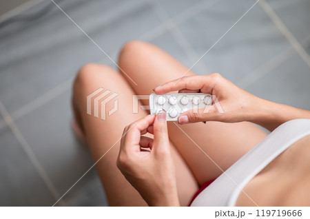 A close-up of a woman in pajamas sitting on a toilet and taking painkillers. A close-up of a woman in pajamas sitting on a toilet and taking painkillers. 119719666