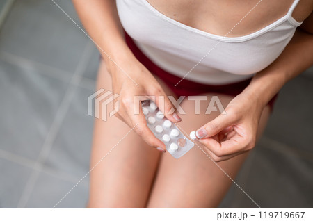 A close-up of a woman in pajamas sitting on a toilet and taking painkillers. A close-up of a woman in pajamas sitting on a toilet and taking painkillers. 119719667