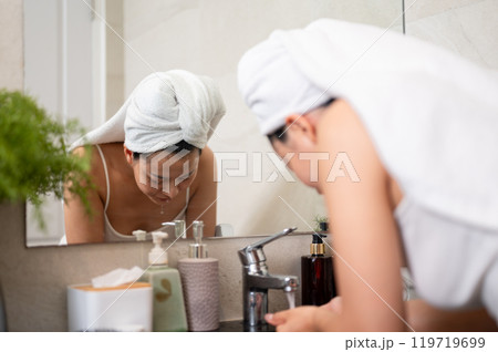 A beautiful Asian woman is washing her face at a bathroom sink after her shower. 119719699