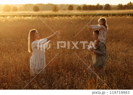 A family of four is walking through a field of tall grass 119719983