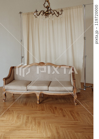 A wooden couch is sitting in front of a white curtain 119720000