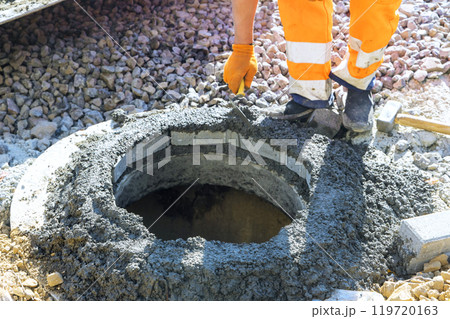 Forefront, fresh concrete is being applied to fix blocks at highest edge of manhole for underground utilities well 119720163