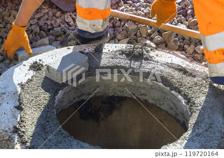 Fresh concrete is being poured to bind blocks forming top section of underground utility manhole 119720164