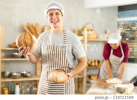 Happy young guy baker posing with basket of freshly baked bread in bakery Happy young guy baker posing with basket of freshly baked bread in bakery 119721589