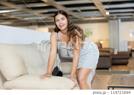 Young woman carefully examines sofa before buying and checks elasticity of surface with hand 119721694
