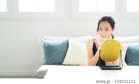 室内で鏡を見てスキンケアする女性 119722111