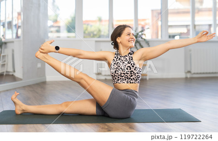 Young positive coach girl in activewear doing stretching exercises during training yoga in sports club 119722264