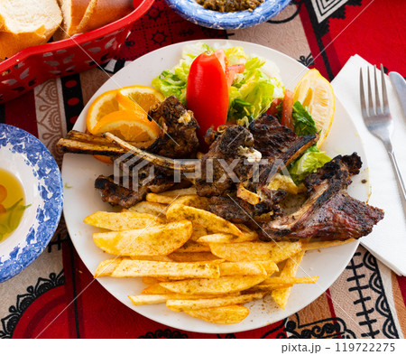 Delicious browned grilled lamb ribs served with crispy french fries and lettuce with tomato on plate, decorated with lemon. Delicious browned grilled lamb ribs served with crispy french fries and lettuce with tomato on plate, decorated with lemon. 119722275